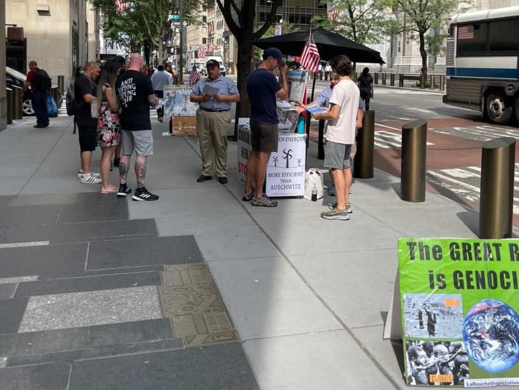 Conspiracy theorists chat with passers-by as swastika poster hangs nearby