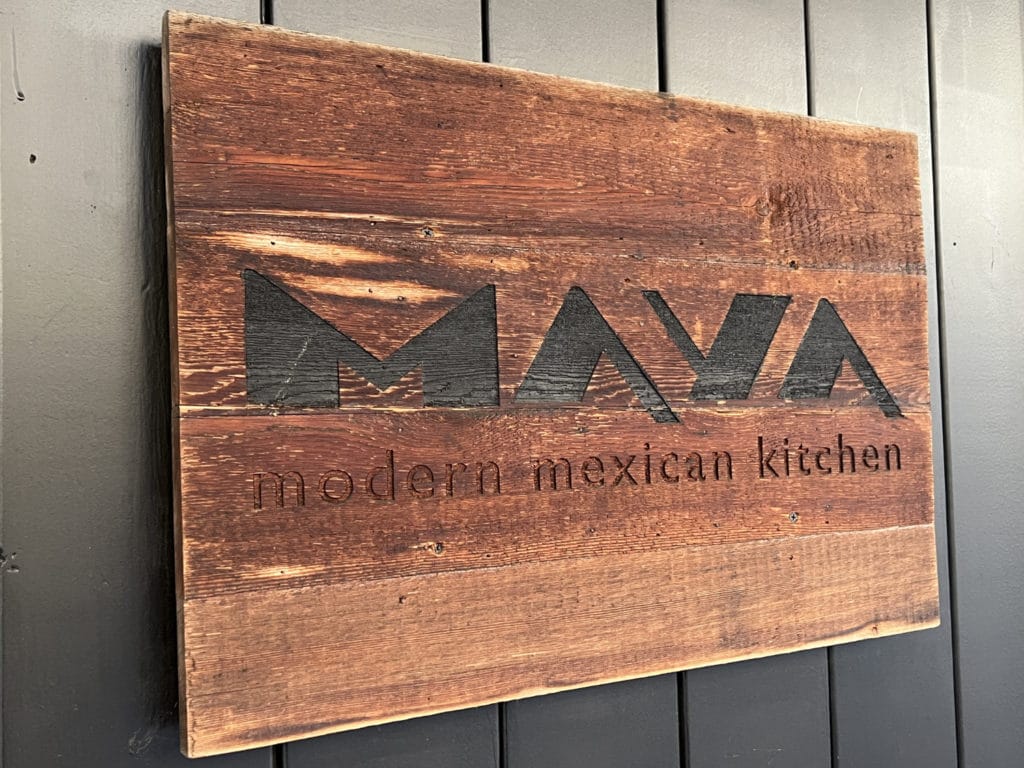 Photo shows a wood sign with the words "MAYA modern mexican kitchen" engraved in it.