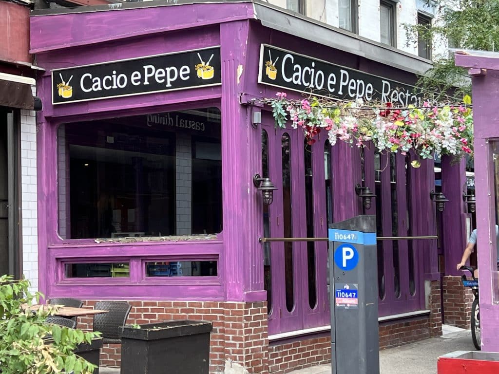 Photo shows a three-quarter view of a restaurant painted a bright purple with black signs featuring white writing reading "Cacio e Pepe."