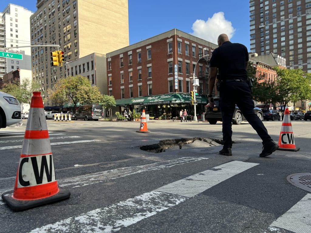 NYPD officer leans over to look inside the sinkhole | Upper East Site