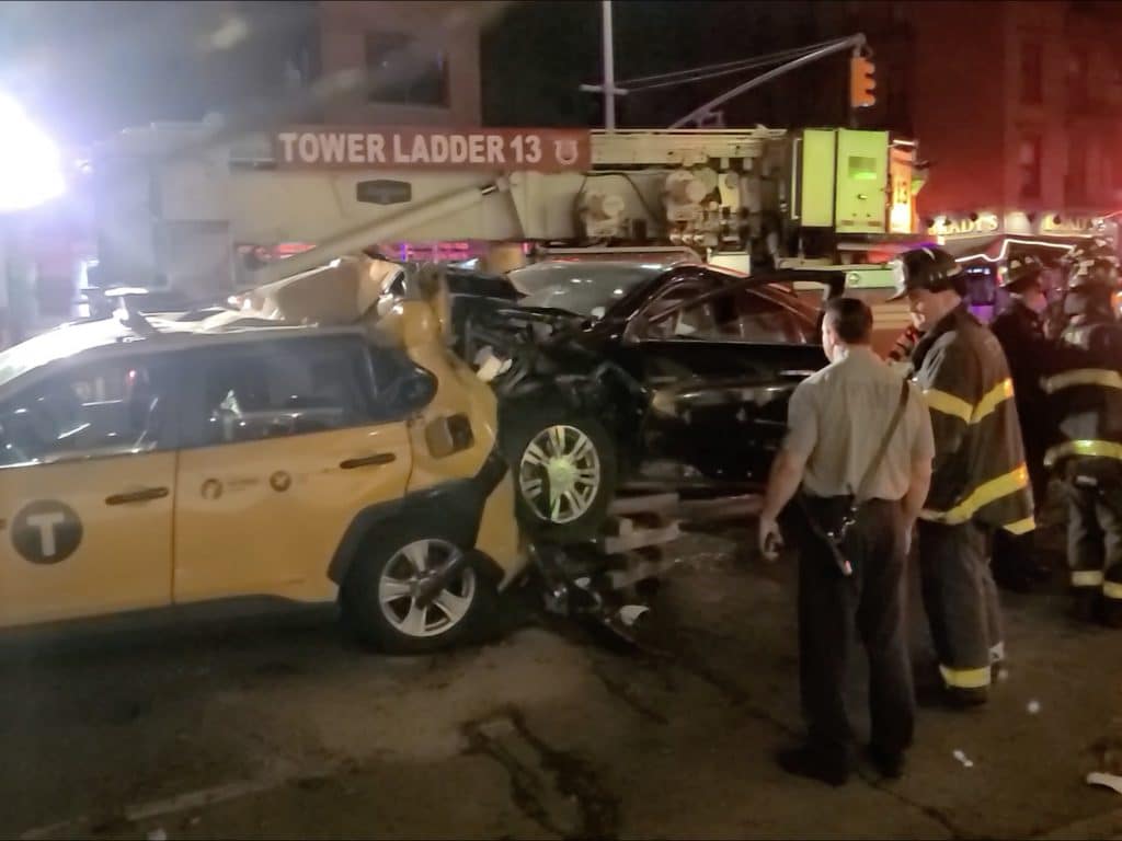 Firefighters stabilize the black Cadillac after crashing on top of the taxi