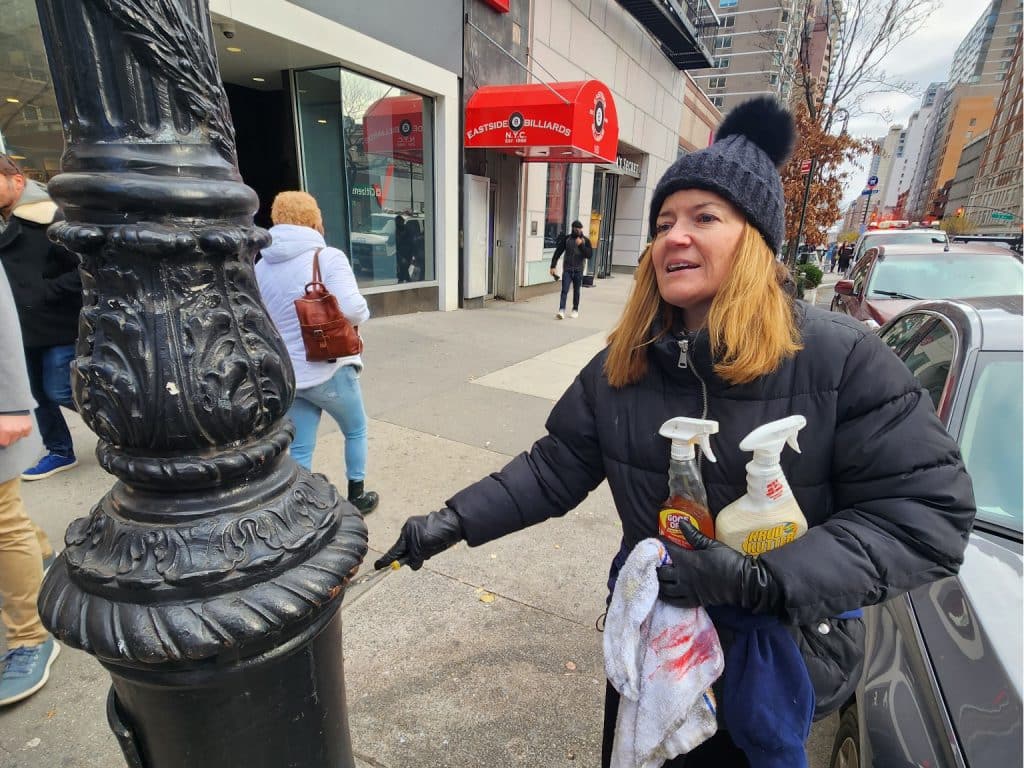 A volunteer removes stickers from a lamp post on East 86th Street