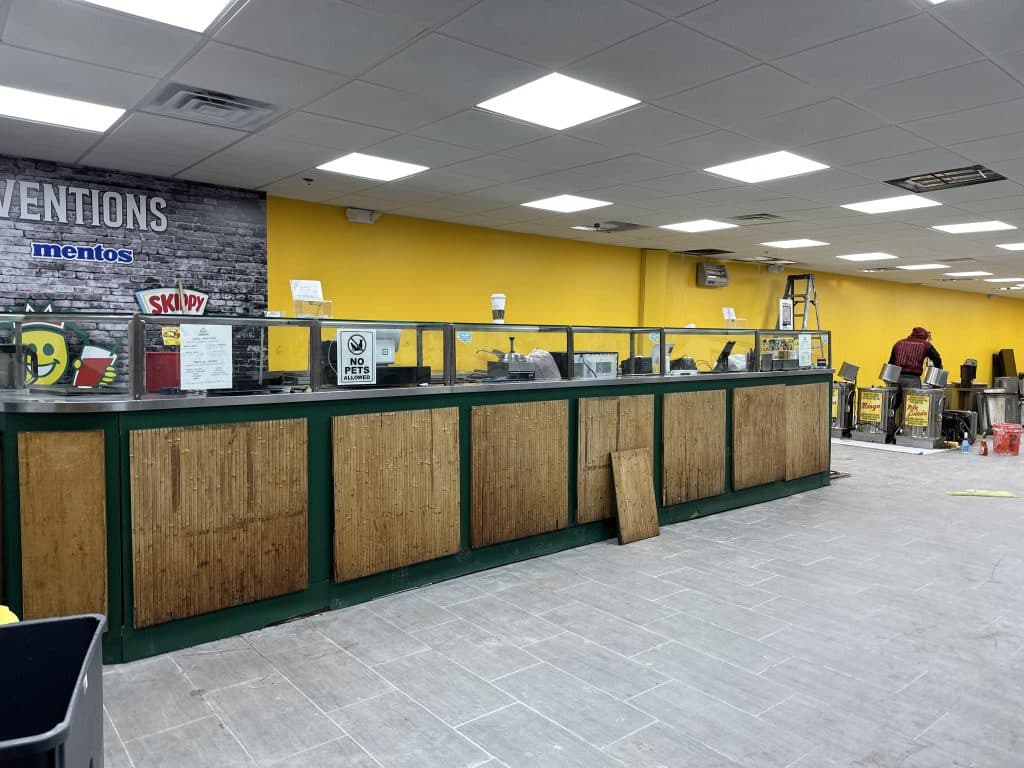 Photo shows the original green and wood paneled Papaya King counter in the new space with yellow walls and grey tile floors.