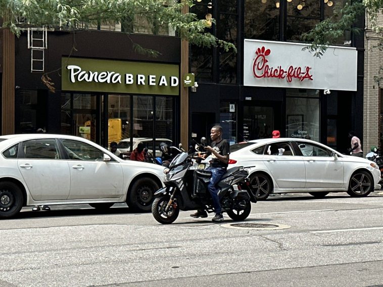 A delivery worker on an unregistered moped rides against traffic on Third Avenue
