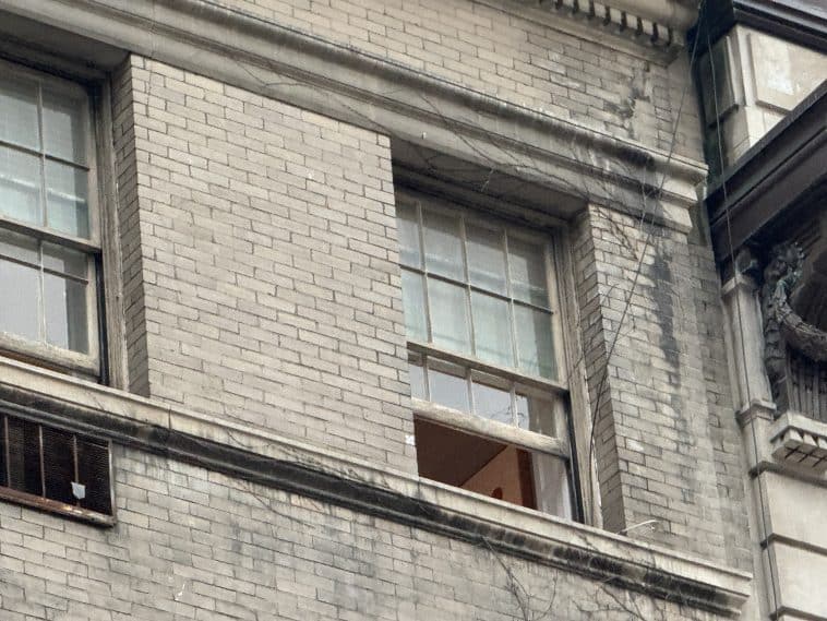 Photo shows a top-floor window of a grey brick building with the window open one third of the way.