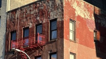Photo shows a the top 1.5 stories of a red brick apartment building in a state of disrepair with a patchwork of facade repairs.