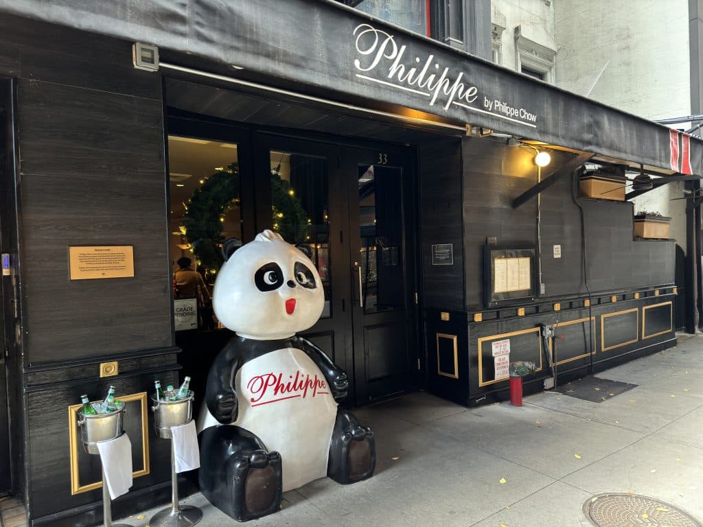 Photo shows a black restaurant storefront from an age with a large panda statue with the name Philippe written in script across its chest.