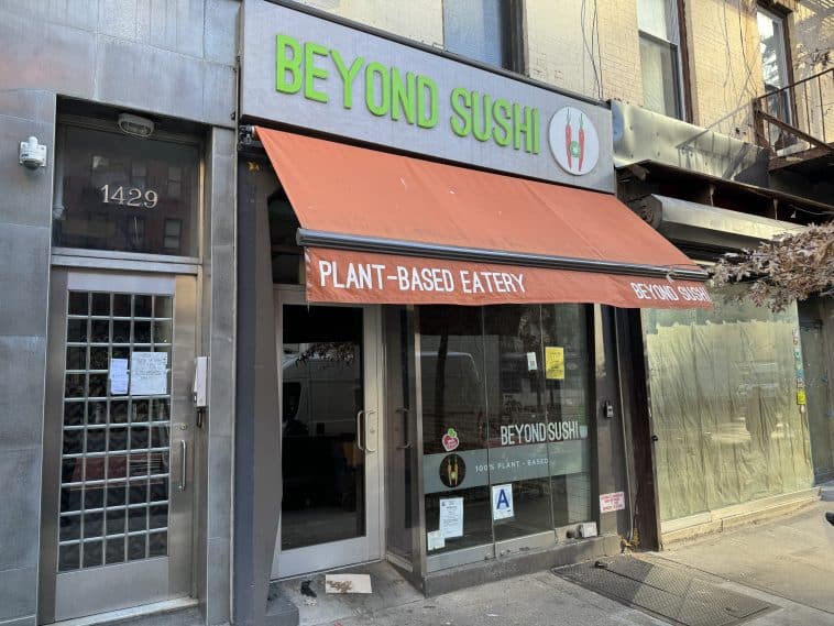 Photo shows Beyond Sushi's glass storefront with an orange rolled up awning and an its silver sign with lime green lettering.