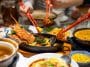 Photo shows a table with several Chinese food dishes and a plate of lobster in the center with three hands using chop sticks to grab a piece