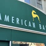 Photo shows a green awning with a yellow dog logo and the name 'AMERICAN BAR' written in white.