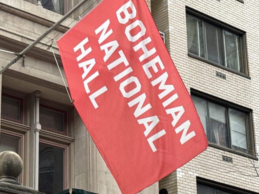 Photo shows a red flag with white writing, reading, 'Bohemian National Hall'