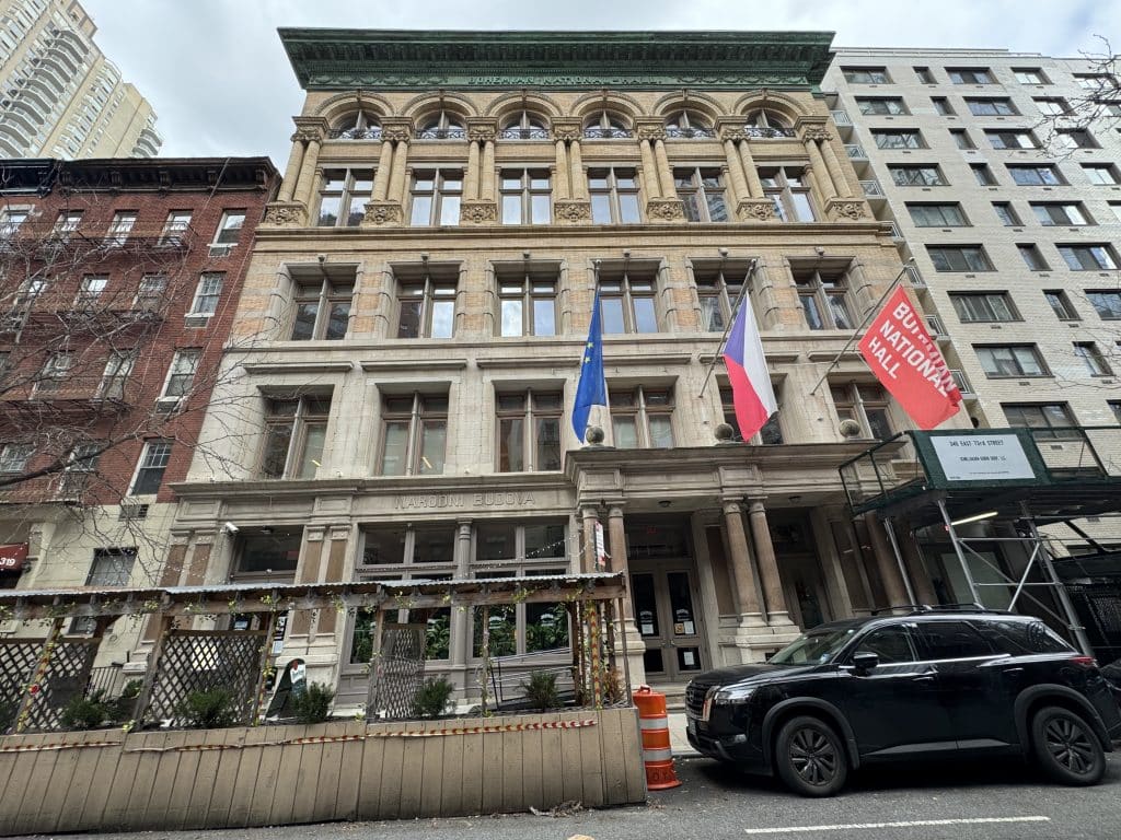 Photo shows a large, five-story historic Upper East Side building with three flags hanging from the facade. 