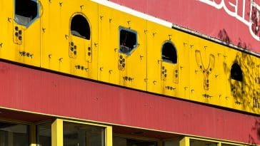 Photo shows a close up of Papaya King's storefront where the neon signage has been removed and rusty holes remain in the yellow metal.