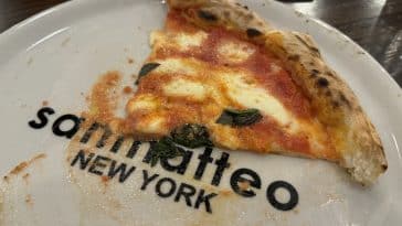 Photo shows one of San Matteo's new custom plates from Italy, featuring its name and logos, with a slice of pizza on it.