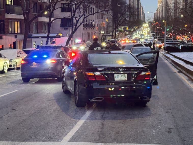 Photo shows a black sedan parked facing northbound in the southbound lanes of traffic, with police vehicles nearby and headlights as far as you can see up the road.