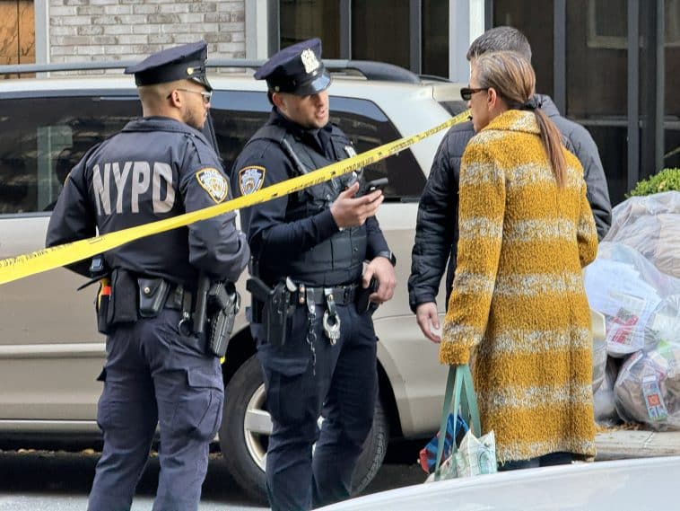 Photo shows two police officers speaking with two members of the public, a man and woman. Yellow police tape separates the two groups.