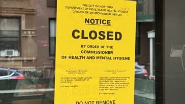 Photo shows a close up a yellow Health Department closure notice stuck to a glass door.