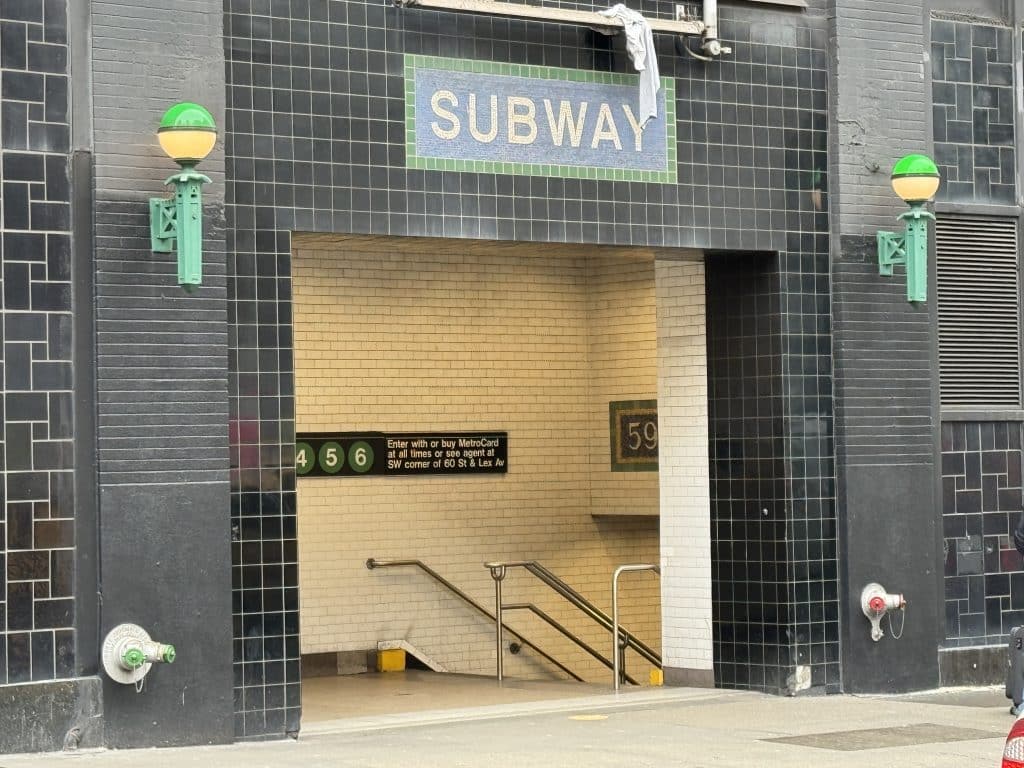 Photo shows a subway entrance in the side of Bloomingdales with black tile out the outside and white tile on the inside leading to a staircase.