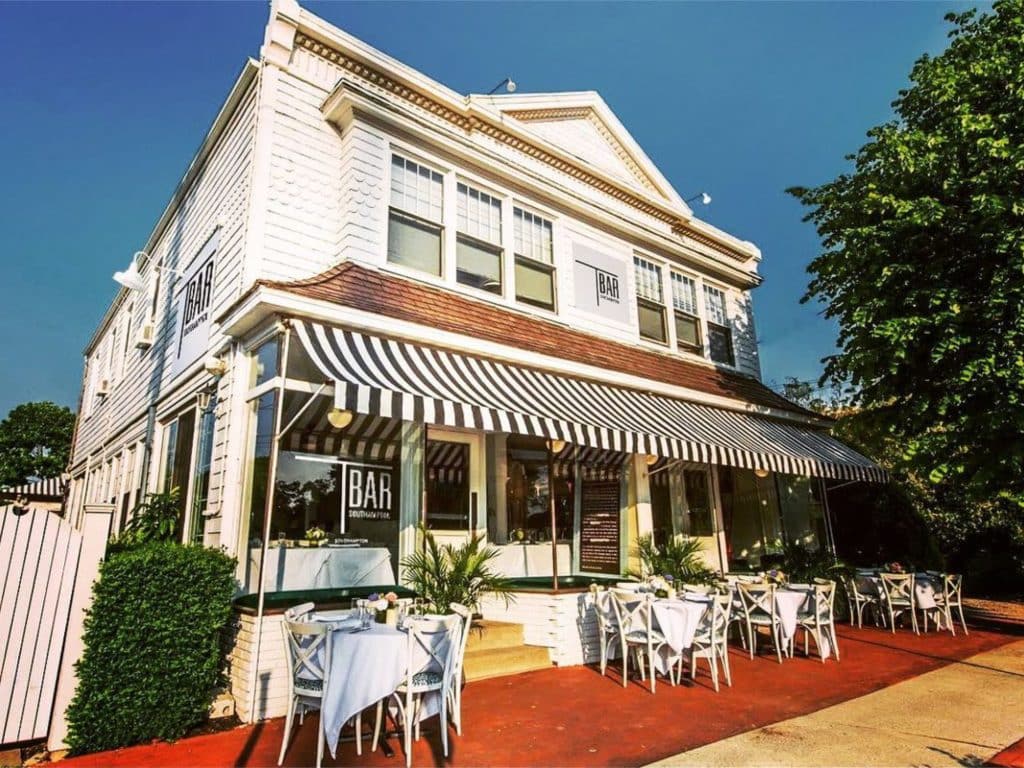 Photo shows a restaurant on the ground floor of a white wood frame two story building.