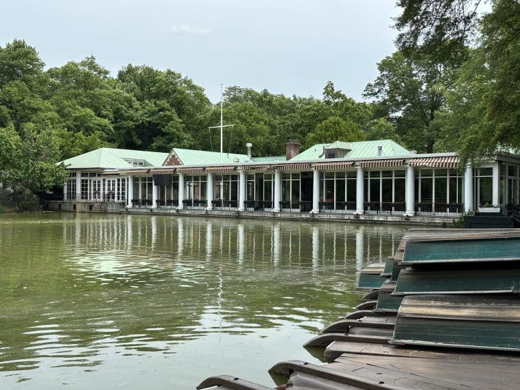 Photo shows a large boat house with a lake in front and boats stacked up on a dock.