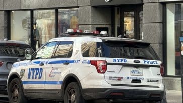 Photo shows an NYPD SUV parked outside a grey storefront with a Nike swoosh one the front.