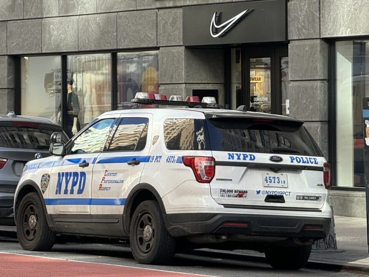 Photo shows an NYPD SUV parked outside a grey storefront with a Nike swoosh one the front.