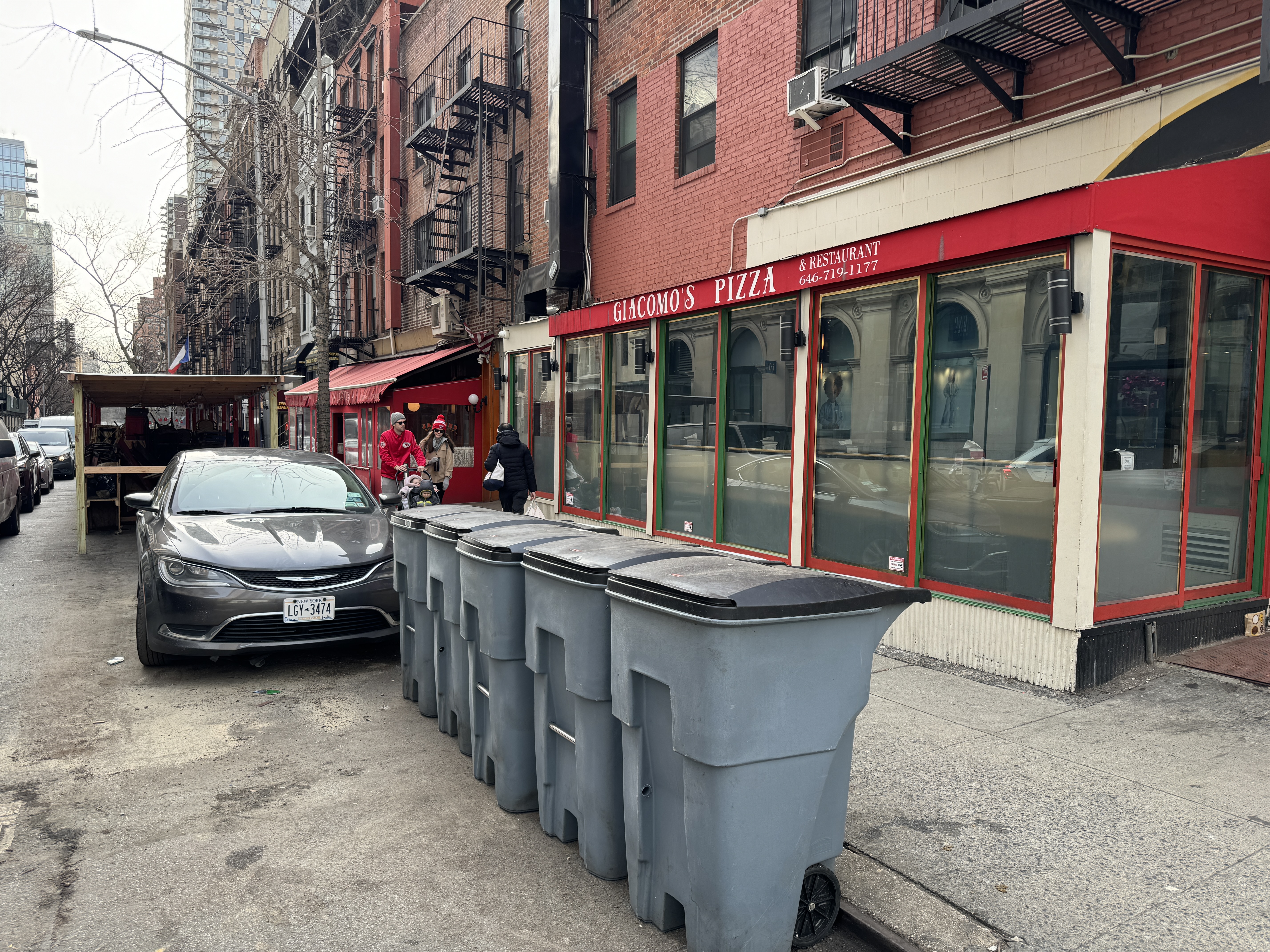 Photo shows commercial garbage cans lined up on the street in front of Giacomo's Pizza where a dining shed used to be.