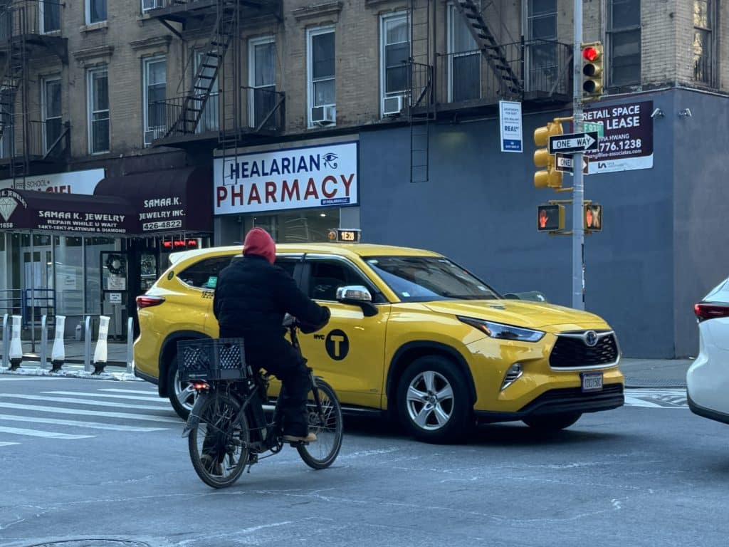 Photo shows a delivery worker on an electric bike riding through a red light into traffic.