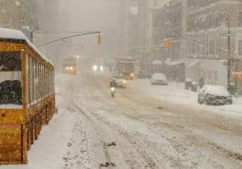 Photo shows a snowy street in new York City with limited vehicles traveling the road.