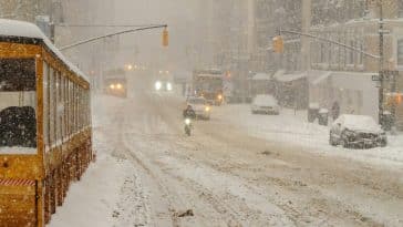 Photo shows a snowy street in new York City with limited vehicles traveling the road.