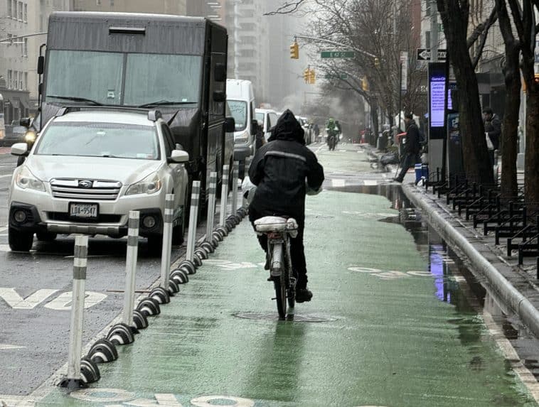 Photo shows a cyclist riding the wrong way down a bike lane in the rain.