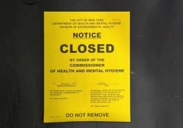 Photo shows a yellow Health Department closure notice on a black door.