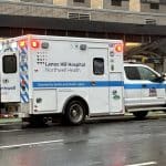 Photo shows an ambulance with its emergency lights on parked in front of a subway entrance in the rain.