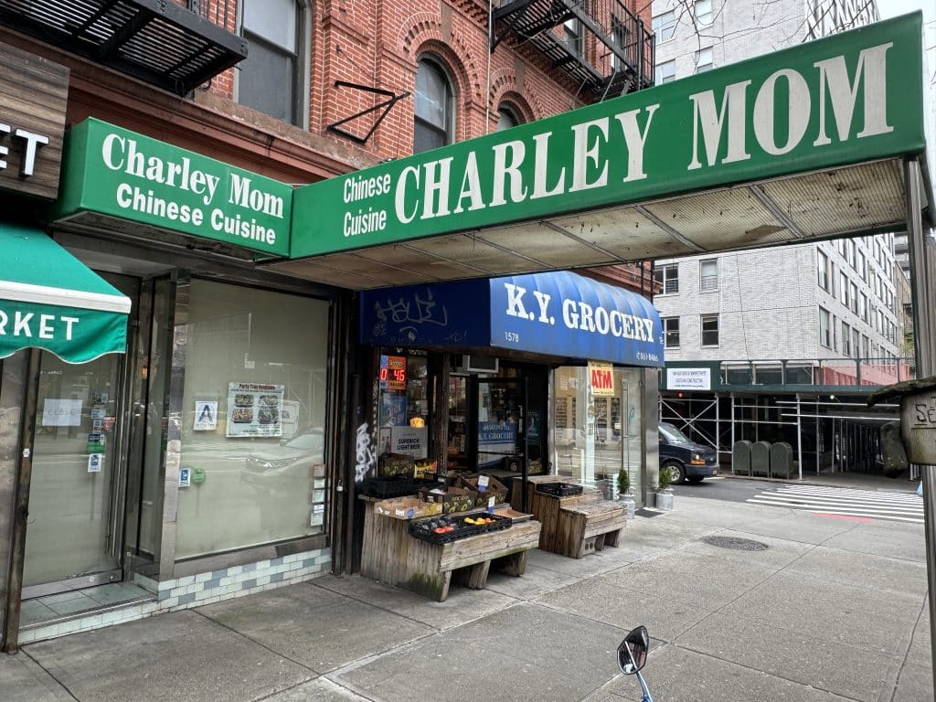 Photo shows an angled view of a storefront with a green awning reading 'CHARLEY MOM' and floor to ceiling windows covered with brown paper.