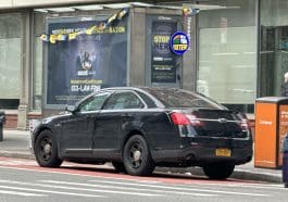 Photos shows a black armored NYPD Ford Taurus parked in front of a newsstand.