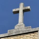 Photo shows a stone crucifix atop a rectory building.