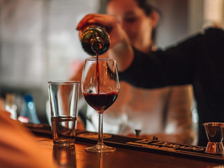 Photo shows a bartender's arm pouring a glass of wine.