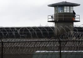 Photo shows razor wire and a prison watch tower.