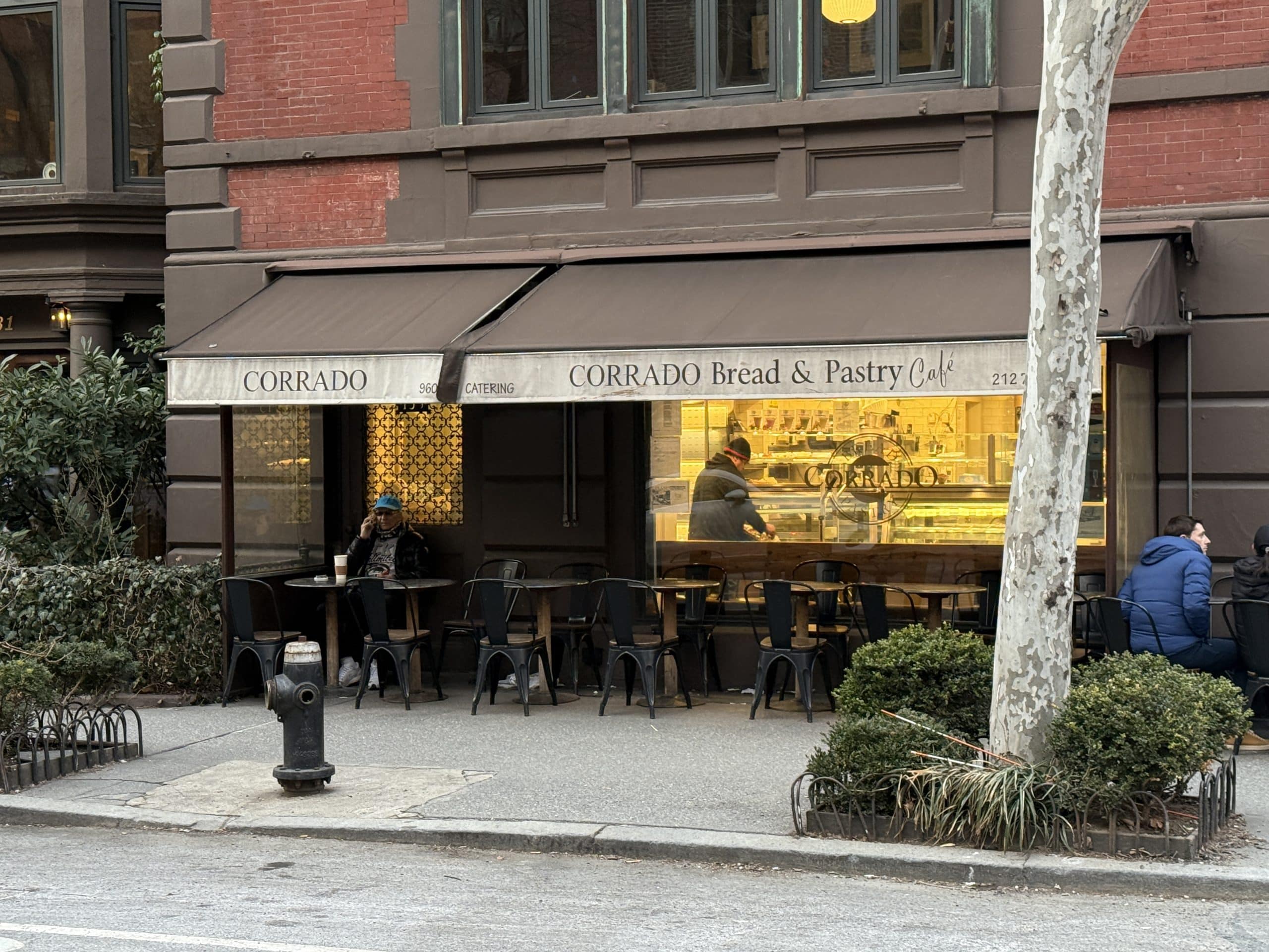 Photo shows a café on the corner of a city street with a beige and brown awning