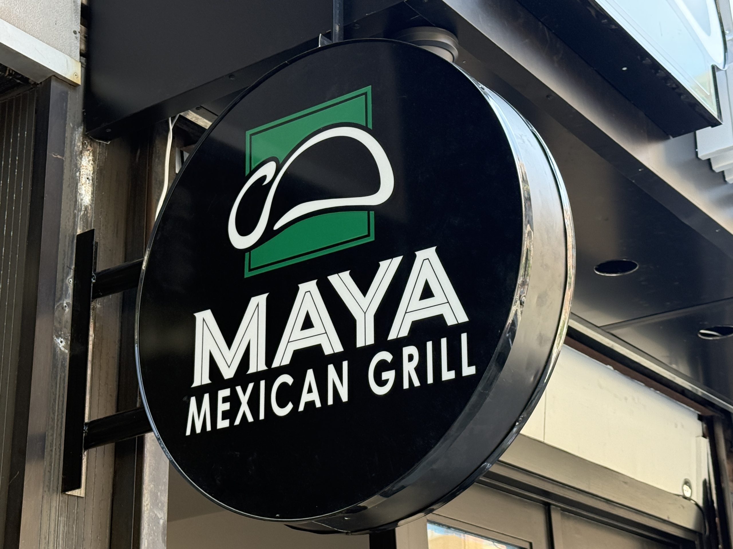 Photo shows a circular black metal sign with a taco logo and the words "MAYA MEXICAN GRILL" in white text.