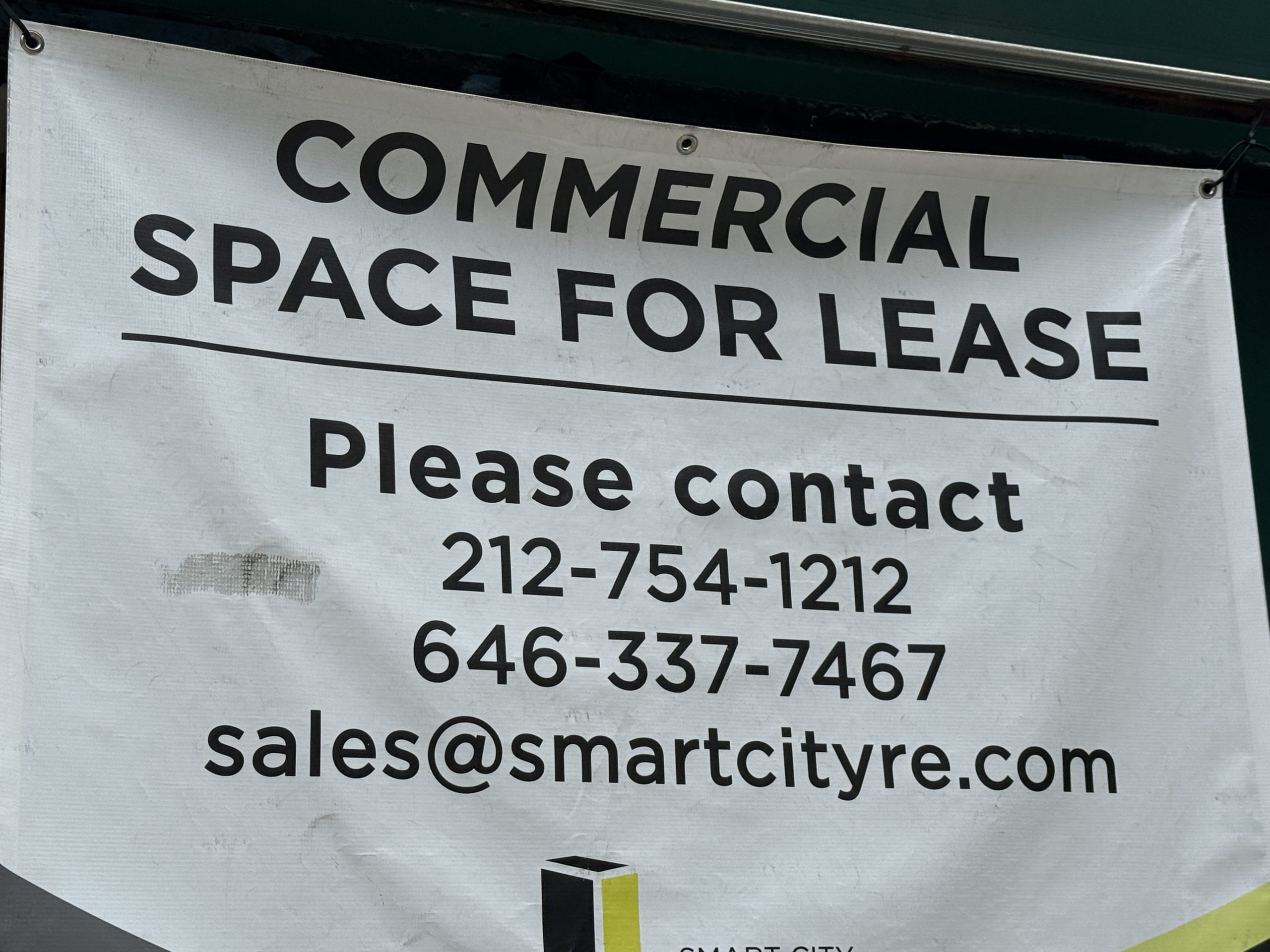 Photo shows a white banner advertising a commercial space for lease in black text.